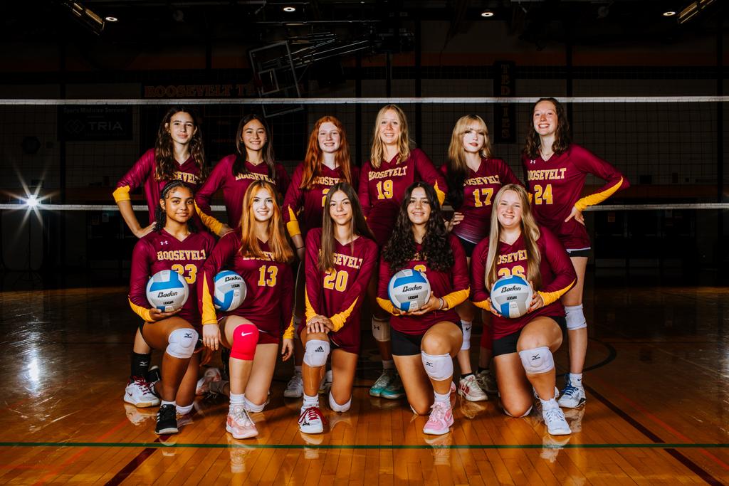 Image of Roosevelt Teddy Volleyball JV team posing for a team picture in Jack Wells Gymnasium. The players wear their maroon uniforms being presented in a dark and dramatic lighting scheme