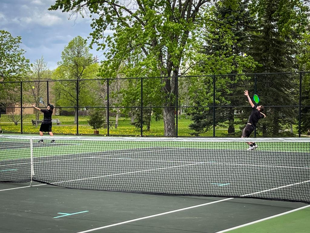 Minneapolis Roosevelt Boys Tennis players #1 and #2 singles players serve at the same time during a match vs Mpls South