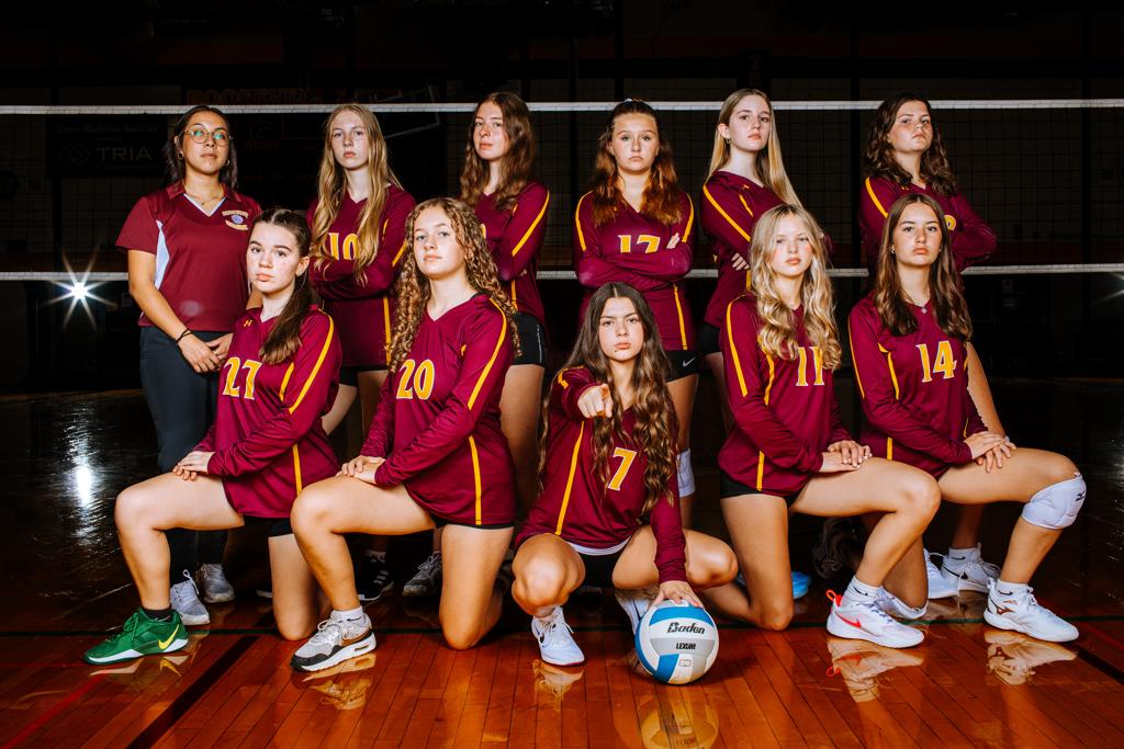 Image of Roosevelt Teddy Volleyball B-Squad team posing for a team picture in Jack Wells Gymnasium. The players wear their maroon uniforms being presented in a dark and dramatic lighting scheme