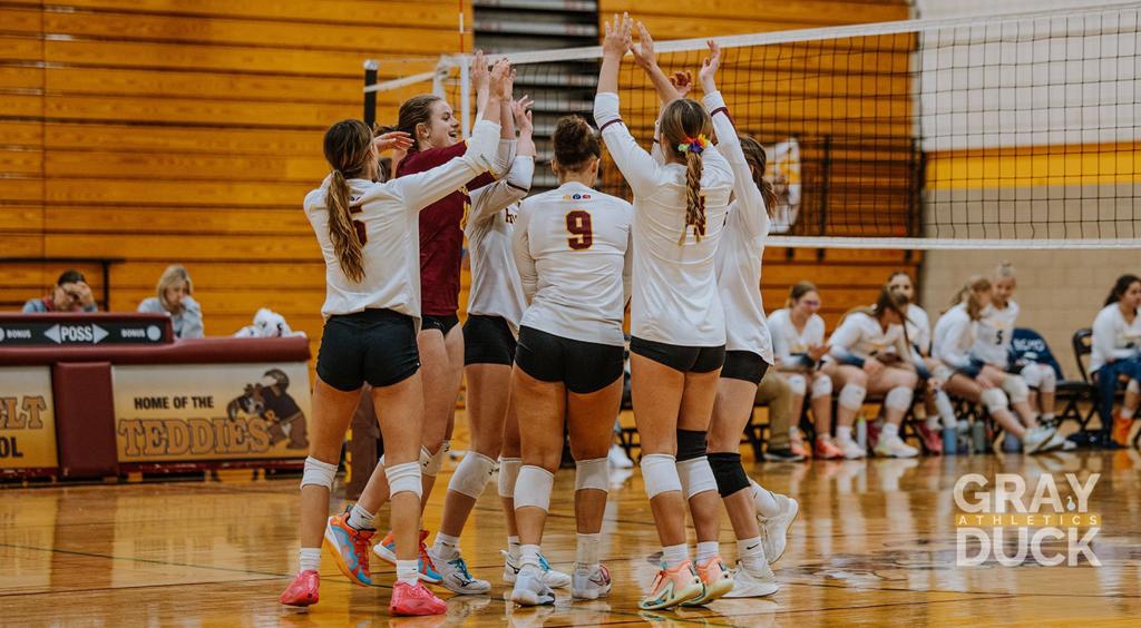 Image of Minneapolis Roosevelt High School Teddy varsity volleyball players grouped at the next celebrating a point win during a match at Jack Wells Gymnasium. 